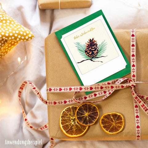 Ein eingepacktes Geschenk mit getrockneten Orangenscheiben und rotem Band, gekrönt von einem Pickmotion Besinnliche Weihnachten | 2er Kleine Klappkarten-Set - festliche Klappkarten ideal für Weihnachtsgrüße.
