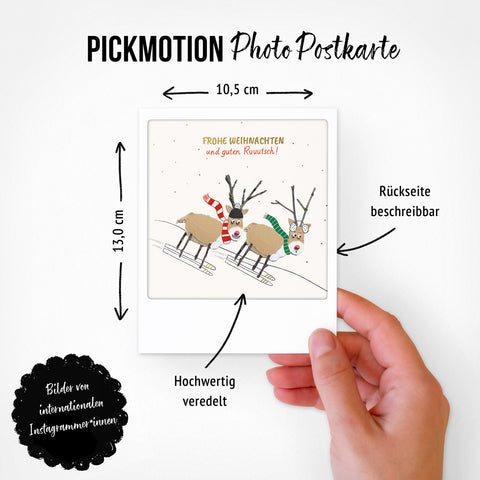 Eine Hand hält ein Pickmotion Zauberhafte Zeit 8er Postkarten-Set mit illustrierten Ski-Rentieren, deutschen Urlaubsgrüßen und festlichen Sprüchen - perfekt als festliche Dekoration.