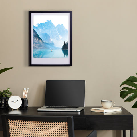 Das gerahmte Kunstposter "blue lake adventures" von Pickmotion über einem modernen Schreibtisch mit Laptop, Uhr, Tasse und Pflanze bringt stilvollen Charakter in Ihr Heimbüro.