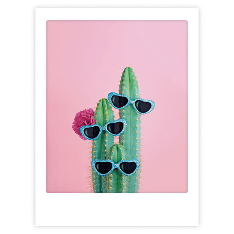 Das "we are family" Kunstposter von Pickmotion zeigt einen hochgewachsenen Kaktus mit drei Armen, die jeweils eine blaue, herzförmige Sonnenbrille tragen und sich als stilvoller Charakter vor einem rosafarbenen Hintergrund abheben - ideal für eine auffällige Dekoration.