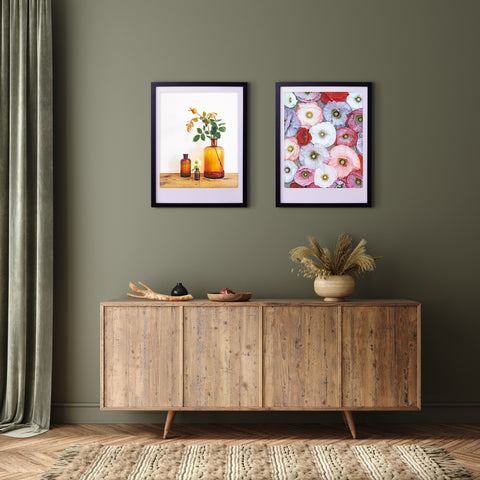 Ein hölzernes Sideboard aus der Mitte des Jahrhunderts mit Dekoration befindet sich unter zwei "blossom together"-Kunstpostern von Pickmotion in maßgefertigten Rahmen an einer olivgrünen Wand.