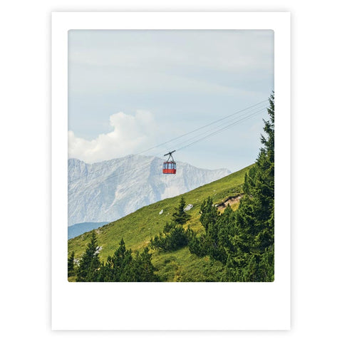 Das Kunstposter "bergauf" von Pickmotion zeigt eine rote Seilbahn, die über einen sattgrünen Hügel und Tannenbäume mit dahinter liegenden Bergen gleitet - eine auffällige Szene, ideal für Ihr Zuhause in einem individuellen Rahmen.