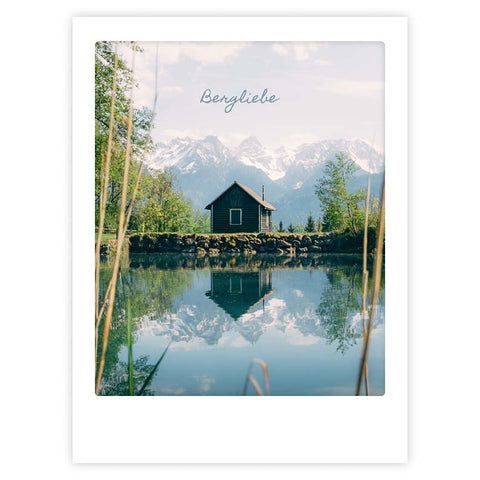 Das Kunstposter "bergspiegel" von Pickmotion zeigt eine kleine Hütte an einem See mit verschneiten Bergen und Bäumen, die sich im Wasser spiegeln, und verleiht jedem Raum stilvollen Charakter.