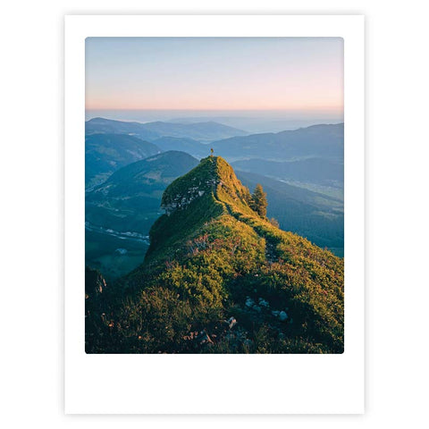 Ein stilvoller Charakter steht bei Sonnenaufgang auf einem grasbewachsenen Bergrücken und blickt auf die fernen Hügel - eine Szene aus "to the top" von Pickmotion, perfekt als Art Poster oder in maßgefertigten Bilderrahmen.