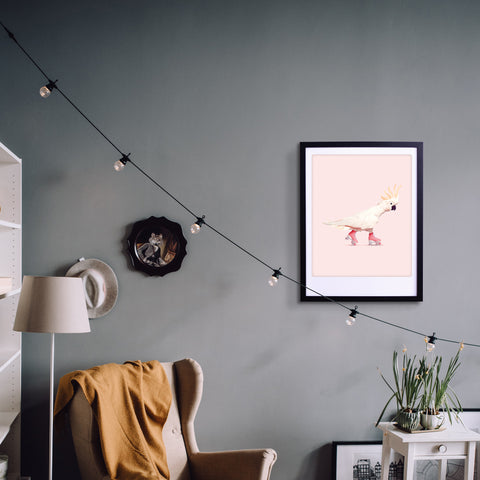In einem gemütlichen Zimmer sorgen ein beiger Sessel, eine gelbe Decke und das "Rock n Roll Birdy"-Kunstposter von Pickmotion in einem individuellen Rahmen an einer grauen Wand mit Lichterketten für stilvollen Charme.