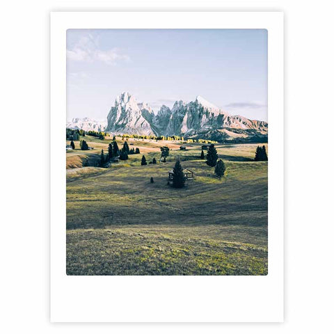 Auf der alm" von Pickmotion: Art Poster mit grasbewachsenen Hügeln, verstreuten Bäumen und einer kleinen Hütte unter einem klaren Himmel - stilvoller Charakter, ideal für maßgefertigte Bilderrahmen.