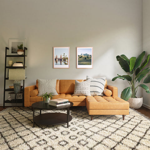 Ein modernes Wohnzimmer mit gelbem Sofa, gemustertem Teppich, Pflanzen und "auf der alm" Wandkunst von Pickmotion in maßgefertigten Bilderrahmen für stilvollen Charakter. Ein schwarzer runder Couchtisch vervollständigt den Look.