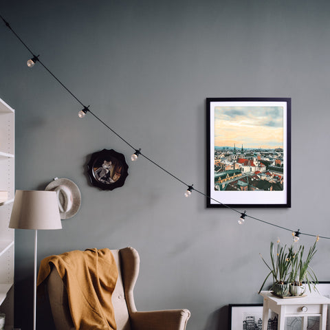 Gemütliches Wohnzimmer mit dem Stadtbild "blick über die stadt" von Pickmotion, einem Sessel, einer Lampe und Lichterketten, die der grauen Wand stilvollen Charakter verleihen.