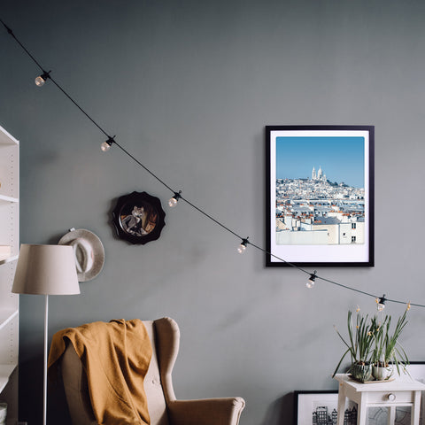 Gemütliches Zimmer mit einem Sessel, Stehlampe, dem Kunstposter "Die Frau in Weiß" von Pickmotion in einem maßgefertigten Bilderrahmen, Lichterketten und Topfpflanzen für stilvollen Charakter.