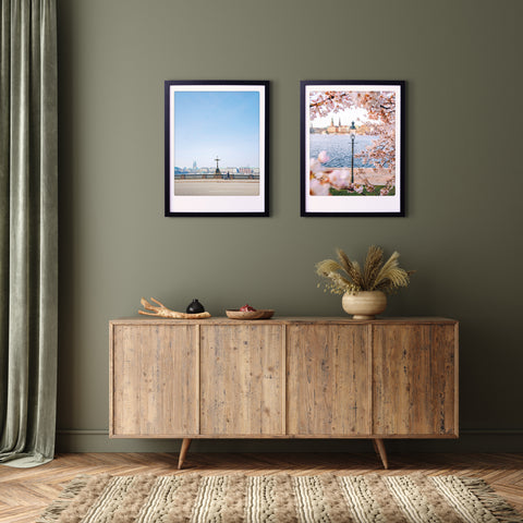 Ein hölzernes Sideboard mit Dekor sitzt unter zwei "alsterspaziergang"-Rahmen von Pickmotion an einer olivgrünen Wand und sorgt für perfekte Instagram-Momente.
