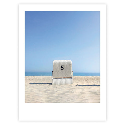 Ein weißer Strandkorb mit der Aufschrift 5 sitzt allein am Sandstrand vor blauem Himmel und Meer und verkörpert stilvollen Charakter - "take it easy" von Pickmotion, perfekt als Art Poster oder gepaart mit maßgefertigten Bilderrahmen.
