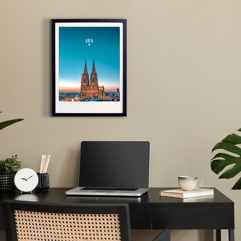 Ein modernes Schreibtisch-Setup mit Laptop, Notebook und der "blauen Stunde in Köln" von Pickmotion - einem gerahmten Foto des Kölner Doms - verleiht dem Arbeitsplatz mit maßgefertigten Bilderrahmen einen eleganten Charakter.
