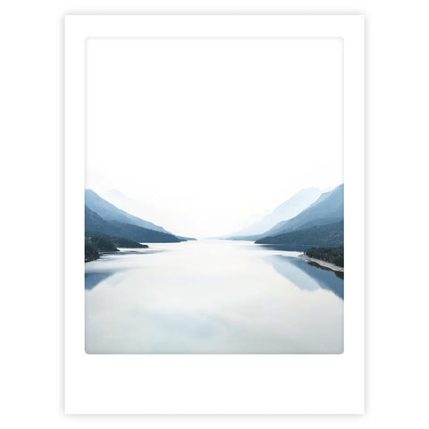 So weit das Auge reicht" von Pickmotion: Ein minimalistisches Foto eines ruhigen Sees, eingerahmt von Bergen unter einem hellen Himmel - ein internationales Motiv, perfekt als Kunstposter oder für maßgefertigte Bilderrahmen.