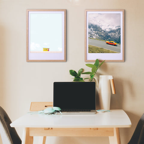 Ein Home-Office-Schreibtisch mit Laptop, Pflanze und "a happy house" Art Poster von Pickmotion in maßgefertige Bilderrahmen, dazu zwei gerahmte Fotos an der Wand darüber.