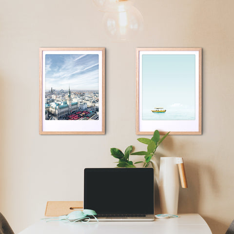 Ein Arbeitsbereich mit einem Laptop, einer Lampe, einer Pflanze und zwei Pickmotion-Rahmen "Smooth Sailing" mit Art Poster an einer beigen Wand verleiht dem Raum einen stilvollen Charakter.