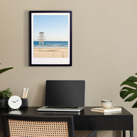 Minimalistischer Arbeitsplatz mit Laptop, Kaffeetasse und dem Kunstposter "a morning at the beach" von Pickmotion, das stilvoll gerahmt über dem Schreibtisch hängt.