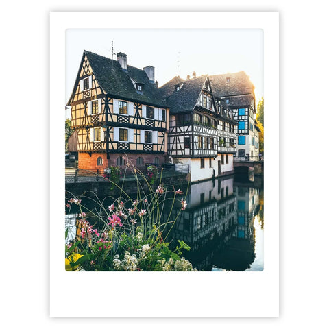 Sommerabend in Straßburg von Pickmotion: Fachwerkhäuser an einem Kanal mit Blumen, die sich im Wasser spiegeln - eine stilvolle Szene, ideal als Kunstposter oder für individuelle Bilderrahmen.