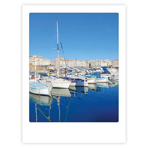 By the harbour" von Pickmotion ist ein Kunstposter, das Segelboote und Yachten in einem Yachthafen mit städtischen Gebäuden unter einem klaren blauen Himmel zeigt - perfekt, um jedem Raum einen stilvollen Charakter zu verleihen.