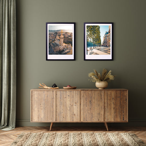 An einer olivgrünen Wand hängen zwei "a sunny day in paris" Art Poster Prints von Pickmotion in maßgefertige Bilderrahmen über einem hölzernen Sideboard mit Dekor und bringen stilvollen Charakter in den Raum.