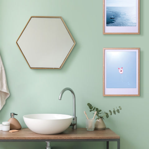 Modernes Badezimmer mit einem sechseckigen Spiegel, einem Waschbecken und zwei Pickmotion "Ballonschwein"-Kunstpostern in stilvollen Rahmen an einer mintgrünen Wand.