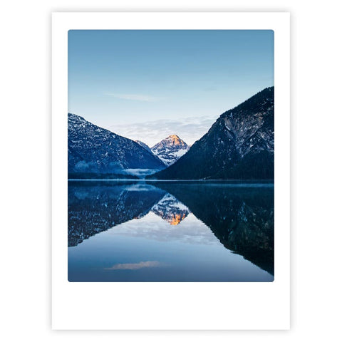 Ein schneebedeckter Berg spiegelt sich in einem ruhigen See zwischen bewaldeten Hügeln unter einem klaren Himmel - "blue lake" von Pickmotion, ein Kunstposter ideal für maßgefertigte Bilderrahmen.