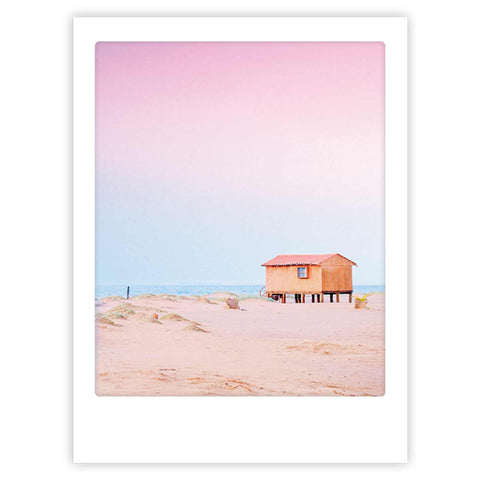 Das Strandhaus von Pickmotion ist eine kleine Holzhütte am Sandstrand unter einem pastellrosa und -blauen Himmel - ein stilvoller Charakter, perfekt zum Ausstellen von Kunstpostern oder maßgefertigten Bilderrahmen.