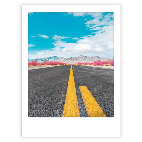 Eine gerade Straße mit einer gelben Linie führt zu fernen Bergen unter einem strahlend blauen Himmel - "Highway" von Pickmotion, ein Art Poster ideal für Fans von internationalem Design.