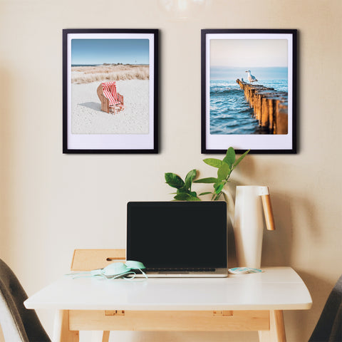 Ein Schreibtisch mit einem Laptop, einer Pflanze und zwei "a seagulls view"-Kunstpostern von Pickmotion in maßgefertigten Rahmen hängen an einer beigen Wand - perfekte Instagrammer-Vibes.
