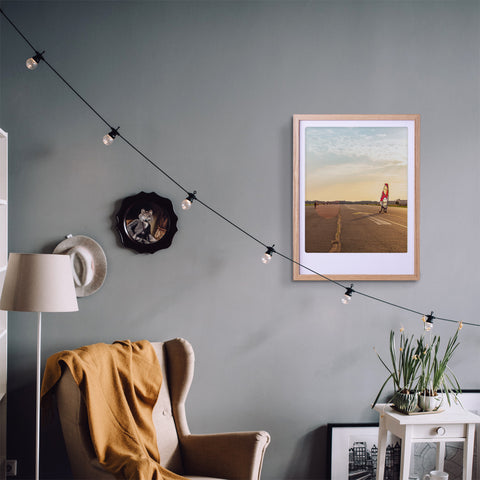 Ein gemütliches Wohnzimmer mit gelber Decke, Wandkunst, Lichterketten und einem gerahmten Pickmotion-Tempelhofer-Feld-Foto - akzentuiert durch maßgefertige Bilderrahmen, die dem Raum stilvollen Charakter verleihen.