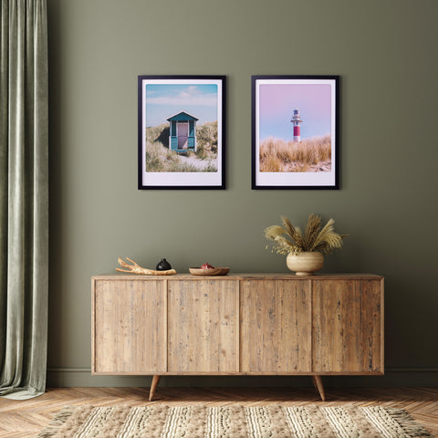 Ein hölzernes Sideboard mit Dekoration, zwei "Sonnenuntergangs-Leuchtturm"-Kunstposter von Pickmotion in maßgefertigten Rahmen und grüne Wände verleihen diesem gemütlichen Raum einen stilvollen Charakter.