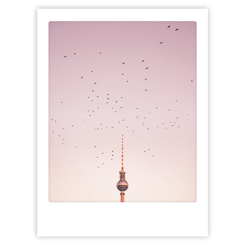 Birds above berlin von Pickmotion: ein Kunstposter mit einem Vogelschwarm über dem Berliner Fernsehturm vor einem zartrosa Himmel - stilvoller Charakter, ideal für maßgefertigte Bilderrahmen.