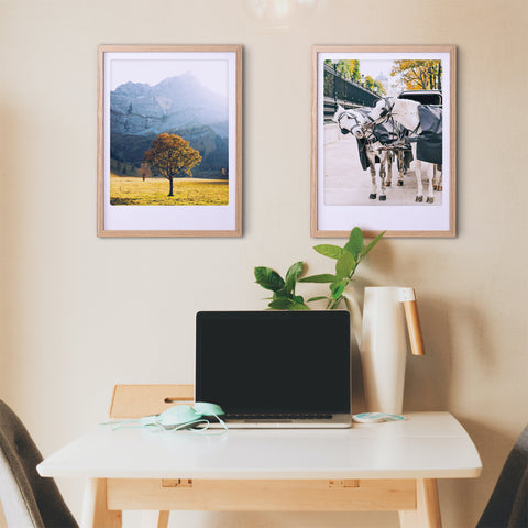 Minimalistischer Arbeitsbereich mit Laptop, Pflanze und zwei Pickmotion maßgefertigten Bilderrahmen - einer mit dem Kunstposter "Herbstblätter" und der andere mit einer Pferdekutsche - die dem Raum stilvollen Charakter verleihen.