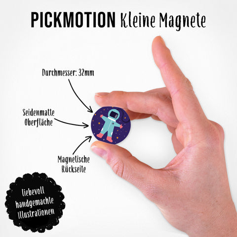 Eine Hand hält einen runden Magneten aus dem Pickmotion-Set "Galaktische Anziehungskraft | Magnet Set | 5 Magnete S", das mit Astronauten-Illustration als originelle Dekoration für jedes Zuhause beworben wird.