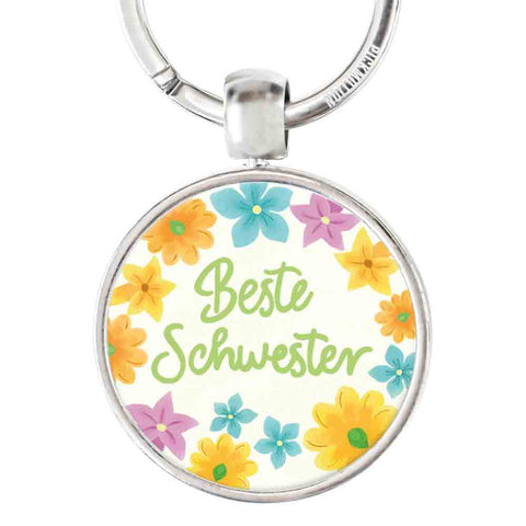 Runder Edelstahl-Schlüsselanhänger von Pickmotion mit "beste Schwester" im Reliefdruck und bunten Blumen am Rand.