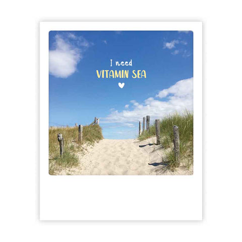 Ein Sandweg führt zum Strand unter blauem Himmel, mit dem Text "i need vitamin sea" von Pickmotion - eine ideale Postkarte oder ein Sofortbild im Insta-Stil, um die Stimmung am Meer zu teilen.