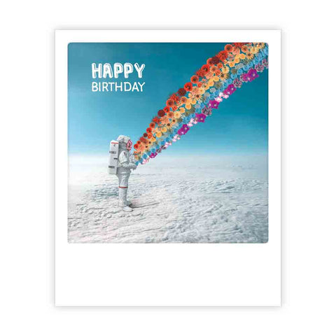 Eine Pickmotion-Geburtstagspostkarte im Sofortbild-Stil zeigt einen Astronauten in einer Schneelandschaft, der bunte Blumen versprüht, mit "Happy Birthday" im Himmel - ideal für einzigartige Grüße oder einzelne Motive.