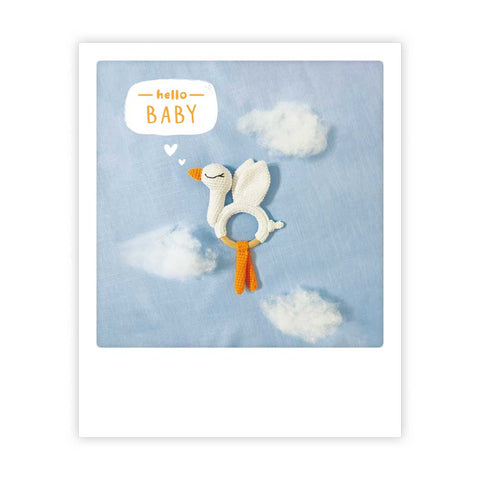 Die Pickmotion "hello baby" Postkarte zeigt eine gehäkelte Storchenrassel auf blauem Wolkenstoff mit "hello BABY" in einer Sprechblase - ideal für Instagram-Liebhaber, die einen verträumten Sofortbild-Stil für süße Grüße wünschen.