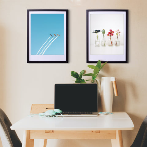 Ein minimalistischer Arbeitsbereich mit einem Laptop auf dem Schreibtisch, zwei "beautiful blossoms"-Kunstpostern von Pickmotion in maßgefertigten Bilderrahmen und einer Pflanze vor einer beigen Wand für stilvollen Charakter.