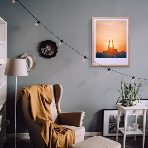 Gemütliches Wohnzimmer mit Sessel, gelber Decke, "Sonnenuntergang in Köln" Art Poster von Pickmotion in einem maßgefertigten Bilderrahmen, Hängelampen, und Zimmerpflanzen für stilvollen Charakter.