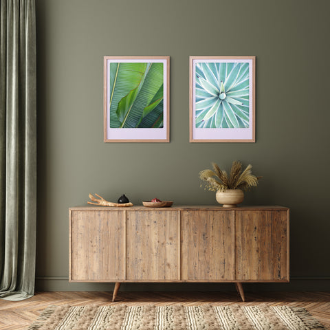 Das "aloe vera" Art Poster von Pickmotion in einem maßgefertigten Bilderrahmen hängt über einem hölzernen Sideboard mit einer Vase und Schalen vor einer grünen Wand.