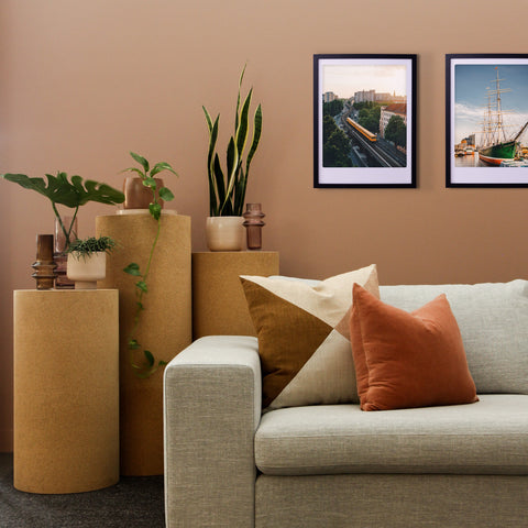 Modernes Wohnzimmer mit beigem Sofa, erdfarbenen Kissen, Pflanzen und einem maßgefertigten Bilderrahmen, der Pickmotion's "through the city" Art Poster auf einer hellbraunen Wand präsentiert und dem Raum einen stilvollen Charakter verleiht.