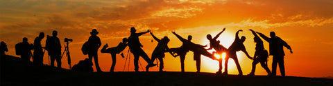 Silhouettierte Menschen posieren und tanzen energisch bei Sonnenuntergang, wenn die Sonne tief am Horizont steht.