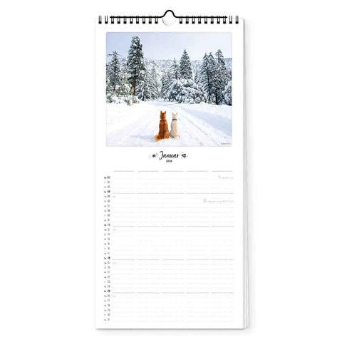Zwei Hunde sitzen auf einem verschneiten Weg in einem Winterwald, abgebildet auf dem Januarblatt des Bunter Hund - Familienplaner (Format 20x42) von Pickmotion - der perfekte Hundekalender für die ganze Familie.