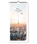Der Pickmotion Berlin - Familienplaner (20x42) 2026 Wandkalender zeigt ein Stadtbild mit Sonnenuntergang und Fernsehturm auf dem Cover - ideal, um die Familie stilvoll zu organisieren.