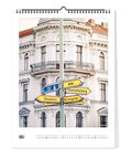 Straßenschilder zu Berliner Bezirken stehen vor einem weißen Gebäude auf der "Juli"-Seite des Berlin-Kalenders (Format 30x40) von Pickmotion - ideal für Fans von minimalistischem Design in ihrer Wandkalender-Kollektion.