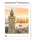 Das Pickmotion Hamburg - Kalender (30x40) zeigt einen steinernen Uhrenturm mit grüner Kuppel und Blick auf den belebten Hafen bei Sonnenuntergang, beschriftet mit März, und fängt den nordischen Design-Charme der Hafenstadt ein.