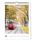 Auf der Seite Pickmotion Wien - Kalender (Format 30x40), März, fährt eine rote Straßenbahn an herbstlichen Bäumen vorbei und fängt die prächtige Architektur und den lebendigen Charme Wiens in atemberaubenden großformatigen Bildern ein.