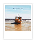 Ein kleines Holzboot ruht auf einem Sandstrand mit "all we need is less" im Himmel, aufgenommen im Sofortbild-Stil von Pickmotion - ideal für Instagram-Fans oder als minimalistische Postkarte.
