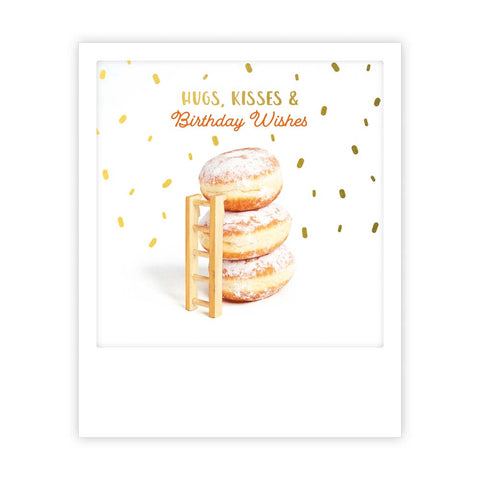 Ein Stapel von drei gepuderten Donuts mit einer kleinen Leiter und goldenem Konfetti, plus "Umarmungen und Küsse" von Pickmotion - eine fröhliche Postkarte für Geburtstage oder Insta-Inspiration mit verspieltem Sofortbild-Stil.